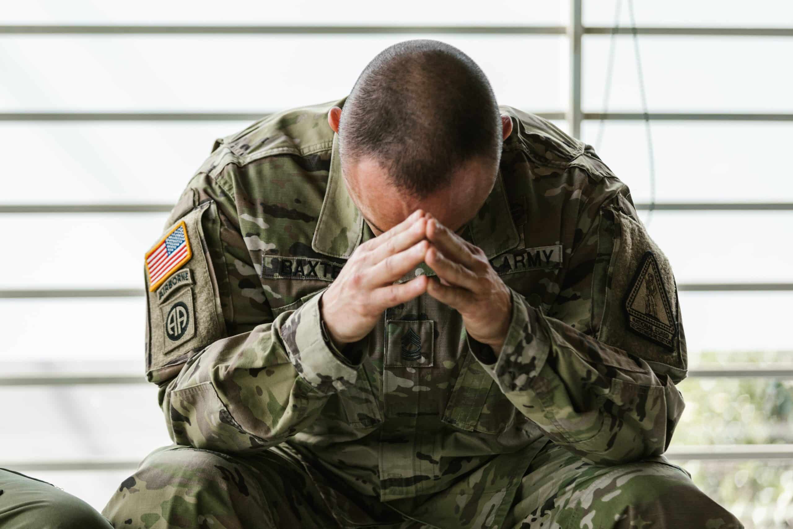 A distressed US soldier in uniform reflecting on his anxiety with his hands on his face, indicative of the need for VA rating for anxiety.