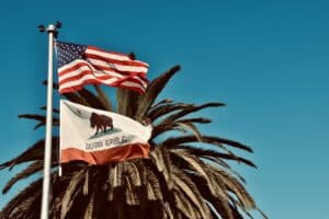 A serene sky with a palm tree frames the US and California flags, highlighting the commitment to veterans' benefits in the Golden State.