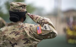 A uniformed military service member, with a VA disability rating for neck pain, saluting with the American flag patch visible on their arm.