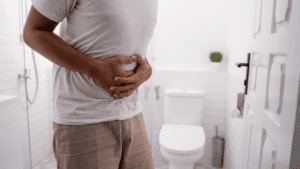 A person clutching their stomach in discomfort stands in a bathroom near a toilet, possibly pondering over the changes in VA disability rating for digestive system issues.