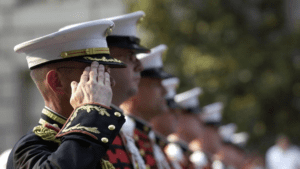 Uniformed military personnel saluting, with one in focus wearing a decorated uniform and white cap, as the 2025 COLA rates are announced