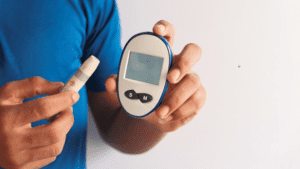 A person holds a blood glucose meter and a lancet against a plain background, illustrating the daily management crucial for understanding VA rating for diabetes.