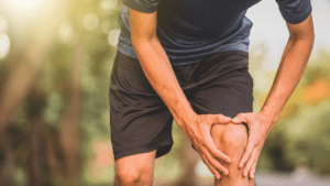 A person in athletic wear holds their knee outdoors, hinting at discomfort or a possible injury. Their expression suggests contemplation about seeking a VA disability for knee pain relief.