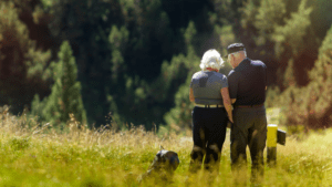 Two elderly people walk together through a grassy field with a dog, surrounded by trees and nature, enjoying the peace and security that dependency and indemnity compensation can provide.