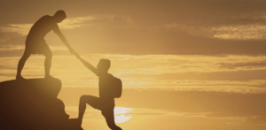 Two people hiking at sunset, with one person helping the other up a rocky slope, both silhouetted against the sky, representing the va rating for depression.