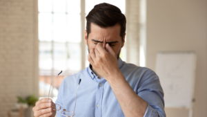 Veteran wearing a light blue button up rubbing his eyes, representing VA disability for dry eyes and eye condition evaluations.